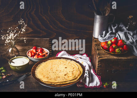 Crepes fatte in casa on dark cucina rustica tabella con le fragole e yogurt in ciotole . In stile country food still life Foto Stock