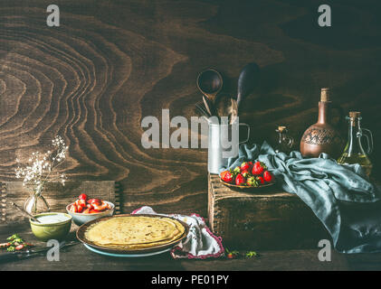 Paese ancora vita con crepes fatte in casa su scuri in legno rustico tavolo da cucina con fragole e yogurt in ciotole . Foto Stock