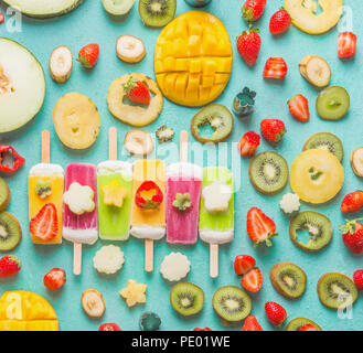 Colorato vari gelati popsicles con freschi fette di frutta e bacche ingredienti su fondo azzurro, vista dall'alto, piatto laici. Tropicale congelato j Foto Stock