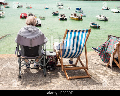 ST IVES, Inghilterra - 19 giugno: OAP matura in seduta sdraio per godersi il sole in St Ives Harbour. In St Ives, Inghilterra. Il 19 giugno 2018. Foto Stock