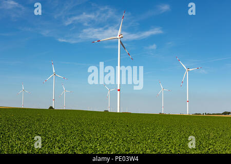 Bella collina verde con il bianco delle turbine eoliche con strisce rosse di generare energia elettrica su un luminoso blu cielo nuvoloso. Foto Stock