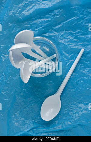Set di bianco cucchiai di plastica in un contenitore di plastica su un blu sacchetto di plastica Foto Stock