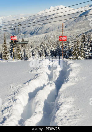 Le tracce nella neve accanto a una ski area segno di confine. Foto Stock