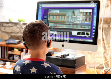 Vista posteriore del bambino che indossa un impianto cocleare digitale tecnologia che guarda lo schermo che gioca un gioco di computer a casa Nel Regno Unito KATHY DEWITT Foto Stock