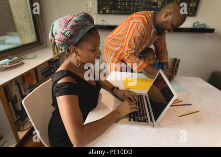 Donna che utilizza computer portatile mentre padre aiutando il suo figlio per disegnare una bozza Foto Stock