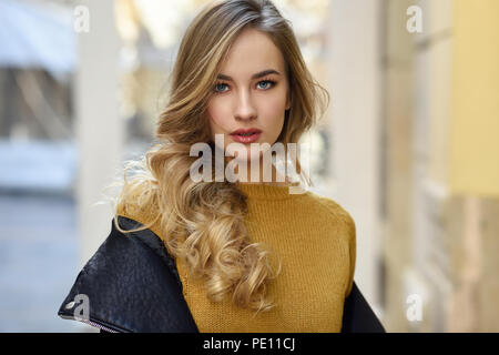 Donna bionda in background urbano. Bellissima fanciulla vestita di nero giacca di pelle e mini gonna in piedi in strada. Pretty donne russe con Foto Stock