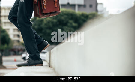 Basso angolo vista di gambe di uomo scendendo le fasi all'esterno. Gambe di uomo che indossa abiti formali e scarpe recanti una borsa da ufficio a piedi giù per la s Foto Stock