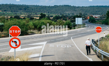 Uomo anziano a piedi con un passato di canna un segno di stop rosso che conduce a un incurvamento autostrada. Metafore concettuali: sempre giovani, non è mai troppo vecchio Foto Stock