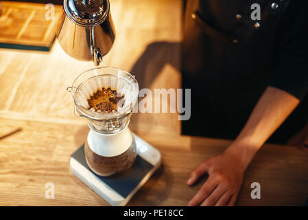 Barista maschio si versa acqua calda nel bicchiere, latte PREPARAZIONE, legno cafe contatore in background. Barman lavora nella caffetteria, il barista fa caffè Foto Stock