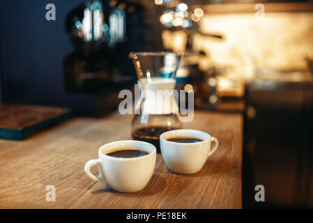 Due tazze di fresco caffè nero sorge sul contatore di legno in espresso cafe, caffetteria interno su sfondo, nessuno Foto Stock