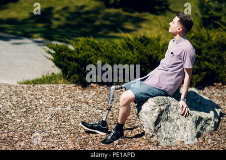 Disabilitato giovane con piede protesi seduta su pietra Foto Stock