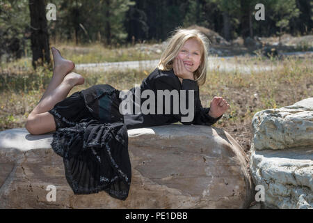 Attraente giovane ragazza bionda, vestiti alla moda in abito nero,, posa sulla grande roccia, guardando la fotocamera. Foto Stock