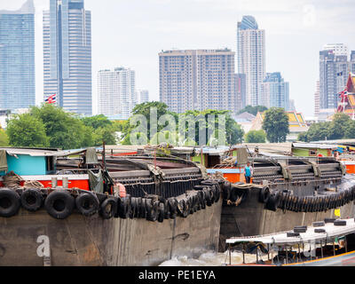 Una chiatta, un fondo piatto nave,per trasportare la sabbia nel fiume Chaopraya con un edificio alto in background, Bangkok, Thailandia Foto Stock