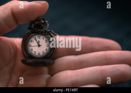 Mano che tiene un orologio da tasca con il tempo che mostra come cinque a ore dodici, concetto di tempo Foto Stock