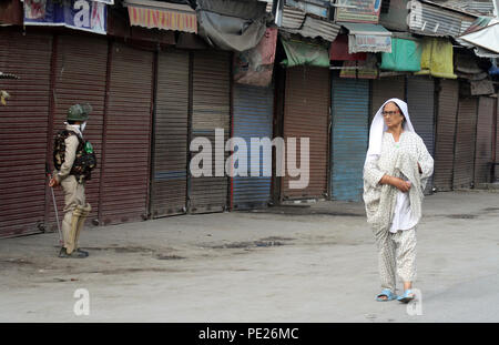 Srinagar, India. Il 12 agosto 2018. Srinagar, Indiano somministrato .KASHMIR .12.Agosto.Un indiano poliziotti sta di guardia accanto a negozi chiuse come le donne del Kashmir passeggiate passato durante .L incontro è iniziato domenica mattina presto tra i miliziani e le forze governative in Batmaloo. area di srinagar .una personale del Jammu e Kashmir Polizia (J&K) è stato ucciso e due di riserva centrale forza di polizia sono stati feriti nell' attentato.©Sofi Suhail/Alamy Live News Foto Stock