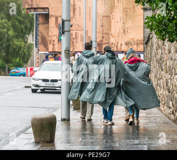 Holyrood, Edimburgo, Scozia, Regno Unito, 12 agosto 2018. Regno Unito: Meteo la pioggia e nebbia come i resti di tempesta Debby colpisce il capitale non scoraggiare i turisti a Holyrood Palace. La gente camminare sotto la pioggia indossando doccia capes Foto Stock