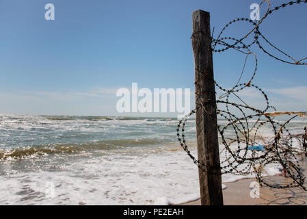 Pilastro di recinzione con filo spinato sulla spiaggia. Vista di barbwire e mare Foto Stock