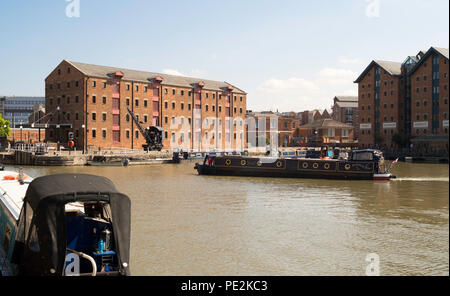 Una barca sul canale che attraversa il bacino principale di Gloucester Docks con il magazzino del Nord e la gru, Gloucestershire, England, Regno Unito Foto Stock