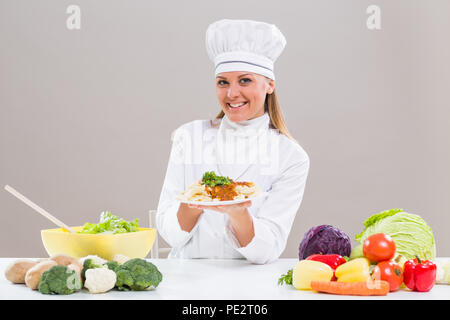 Contenuto chef femmina è seduta al tavolo con il mazzetto di origine vegetale che mostra pasto preparato. Foto Stock