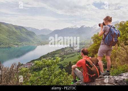 Viaggi e turismo, giovane coppia di viaggiatori con zaini godendo di una vista panoramica del lago, gli escursionisti rilassante sulla cima della montagna Foto Stock