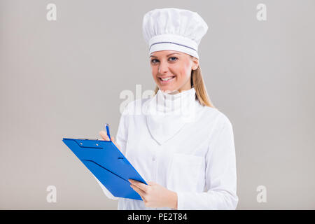 Bellissima femmina chef è in possesso di un libro di cucina e la scrittura di una nuova ricetta. Foto Stock