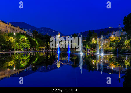 Fontana riflettente sulla Promenade du Paillon, circondato da un verde parco urbano, illuminato con il rosso e il blu delle luci al tramonto a Place Massena Massena o s Foto Stock