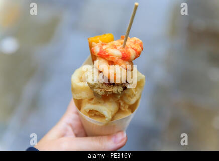 Cibo di strada italiano a Venezia - fritto misto (misto di pesce fritto, calamari o calamari e gamberi) in un cono in movimento Foto Stock