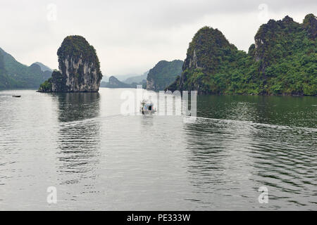 Una piccola barca da pesca in direzione di gamma di isolotti di Halong Bay, Vietnam del Nord, in un giorno nuvoloso. Foto Stock