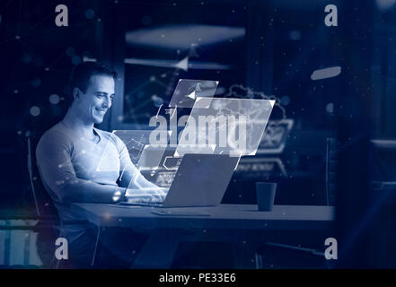 Giovane uomo che lavora sul computer portatile di notte nel buio ufficio. Il designer lavora in un tempo successivo. Foto Stock