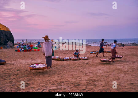 CHAUNG THA, MYANMAR - 28 febbraio 2018: il tramonto è l'elevato tempo per il cibo di strada, fornitori di trasportare le loro merci in cesti su gioghi lungo la spiaggia Foto Stock