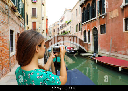 Giovane donna di scattare una foto con la fotocamera mirrorless di canali tradizionali vista di Venezia, Italia Foto Stock