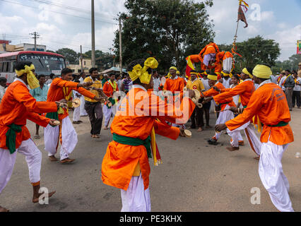 Mellahalli, Karnataka, India - 1 Novembre 2013: Karnataka Rajyotsava Parade. Gruppo di arancione e bianco uomini danza in un cerchio sulla strada. Foto Stock