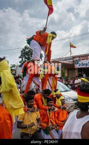 Mellahalli, Karnataka, India - 1 Novembre 2013: Karnataka Rajyotsava Parade. Arancione e bianco maschio placcati acrobati forma di piramide in strada con le automobili Foto Stock