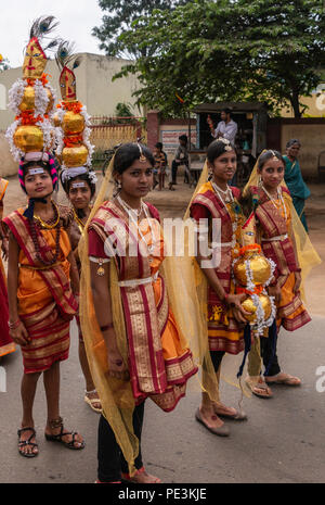 Mellahalli, Karnataka, India - 1 Novembre 2013: Karnataka Rajyotsava Parade. gruppo di vestito ragazze con cappelli giganti. Una posizione dominante di colore arancione, marrone, oro Foto Stock