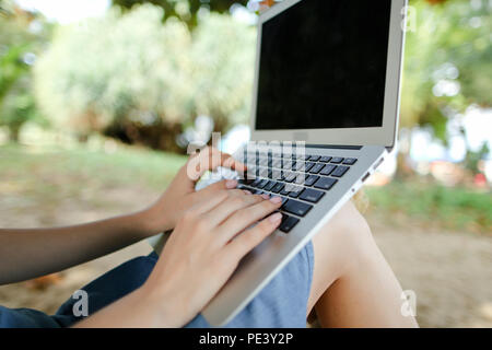 Bella femmina mani con computer portatile con sabbia in background, schermo nero. Foto Stock