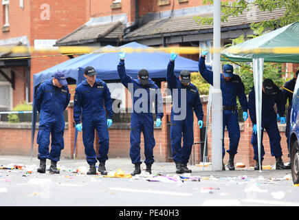 Polizia da la tattica di unità Aiuto effettuare una ricerca fingertip in Claremont Road, Moss Side, Manchester, dove dieci persone, tra cui due bambini sono stati portati in un ospedale dopo le relazioni degli spari a un partito di strada. Foto Stock