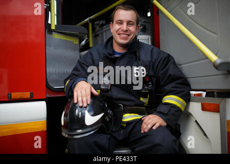 Foto di felice fireman guardando la fotocamera in camion dei pompieri Foto Stock