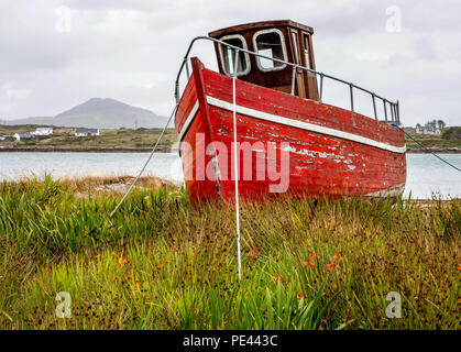 Rosso pesca barca tirata fino al di fuori dell'acqua a Roundstone sulla costa del Connemara in Irlanda occidentale Foto Stock