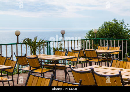 Terrazza con tavoli e sedie di legno con vista sul mare nella soleggiata giornata estiva Foto Stock