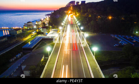 Vista Drone dell'illuminato Matsesta viadotto, pendio di montagna con una fitta foresta e il mare al tramonto, Sochi, Russia Foto Stock