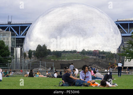 Persone rilassarsi sul prato del La Villette Parco con una vista dello specchio-dome finito La Géode, Parigi, Francia, Foto Stock