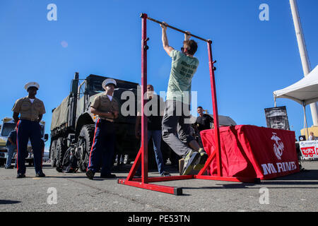 US Marine Corps reclutatori dell'area di San Francisco guarda un visitatore effettuare il pull-up sfida durante una nave statico display su Pier 80 come parte di San Francisco Fleet Week 2015, 10 ottobre. SFFW 15' è un evento della durata di una settimana che unisce un esclusivo programma di training e formazione, riunendo le principali civile soccorritori di emergenza e di crisi navale di forze di risposta di scambio di migliori pratiche incentrate sugli aiuti umanitari aiuto in caso di catastrofe con particolare enfasi sulla difesa sostegno alle autorità civili. Foto Stock