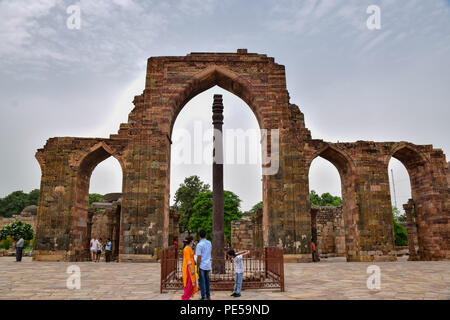 I turisti watche il pilastro di ferro ancora in piedi di fronte alla rovina ingresso struttura arcuata al complesso di Qutub a Delhi in India. Qutub Minar in piedi 73 metri alta a Delhi, è il più alto minareto in mattoni e dall'UNESCO patrimonio dell'umanità. Esso rappresenta la indo-islamica stile architettonico, costruito da Qutb-ud-din Aibak come una vittoria Torre nel 1192 D.C. Foto Stock
