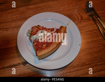 Mangiare fuori un delizioso spessa fetta di tradizionale stile di Chicago al forno ripiene italiana famosa pizza pasto su un Round piastra bianca con argenteria Foto Stock