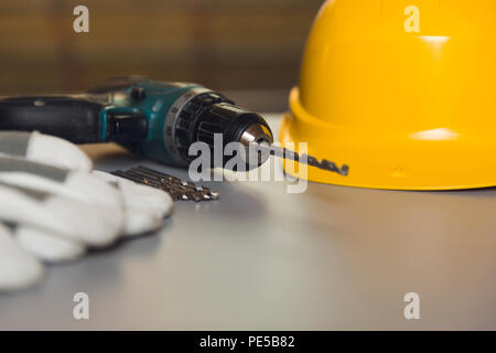 Equipaggiamento standard di sicurezza. Casco giallo, guanti e cacciavite elettrico sulla tabella grigia Foto Stock