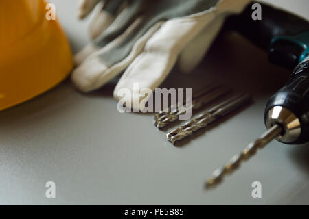 Equipaggiamento standard di sicurezza. Casco giallo, guanti e cacciavite elettrico sulla tabella grigia Foto Stock