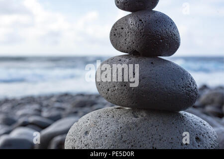 Dettaglio di un equilibrato impilati pietre o ciottoli su una spiaggia con l'orizzonte in background. Foto Stock