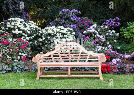 Una panca in legno nel parco, fiori colorati sul retro. Foto Stock