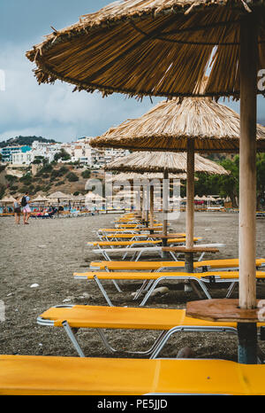 Ombrello di paglia su una spiaggia di sabbia in Grecia. Sedie da spiaggia con ombrelloni su una bellissima spiaggia a Creta. Foto scattata in Grecia. Foto Stock