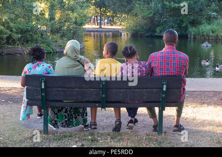 Una famiglia musulmana godetevi la serata di sole su una panchina nel parco in un parco di Londra Foto Stock